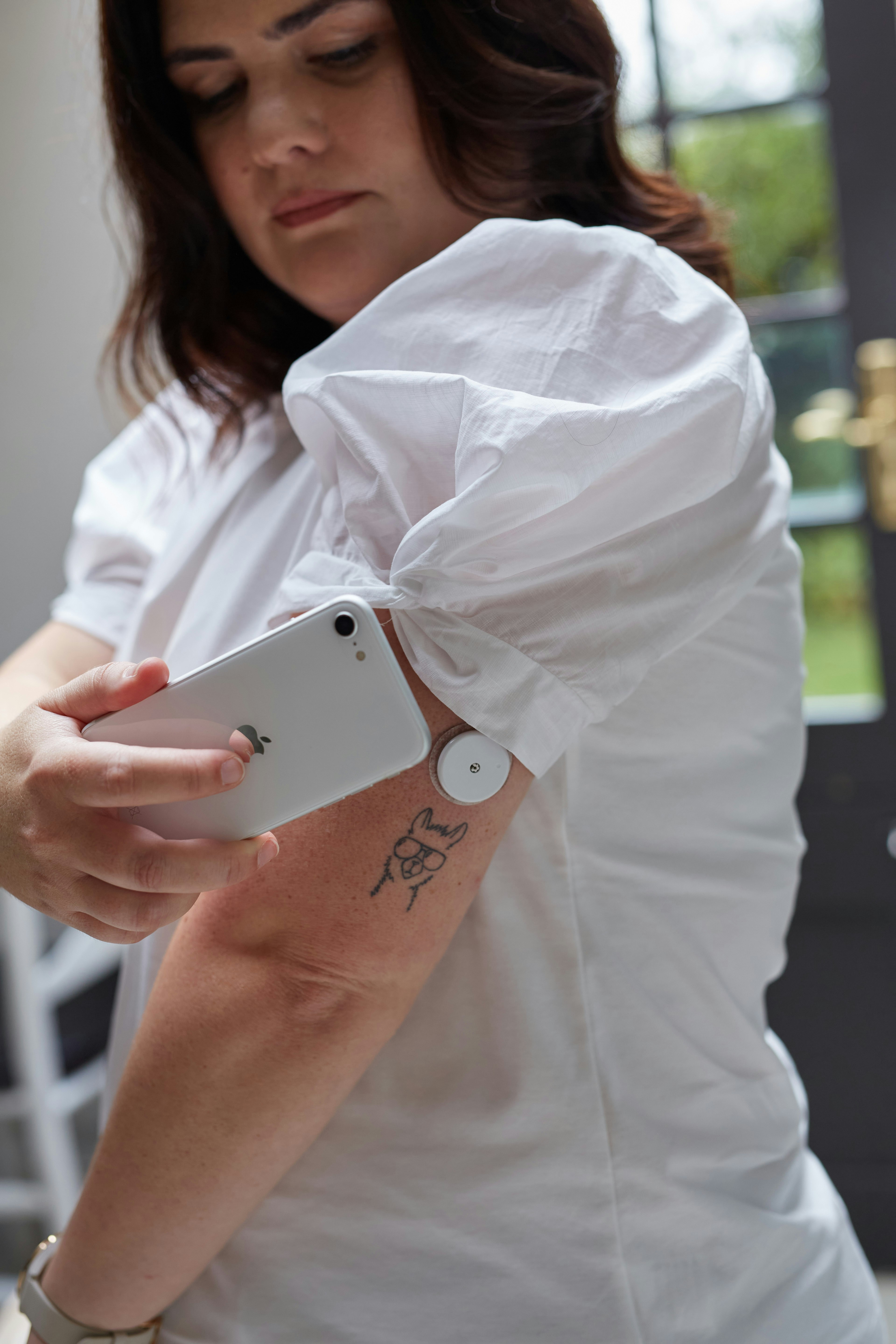 A person wearing a continuous glucose monitor on their upper arm while checking their phone